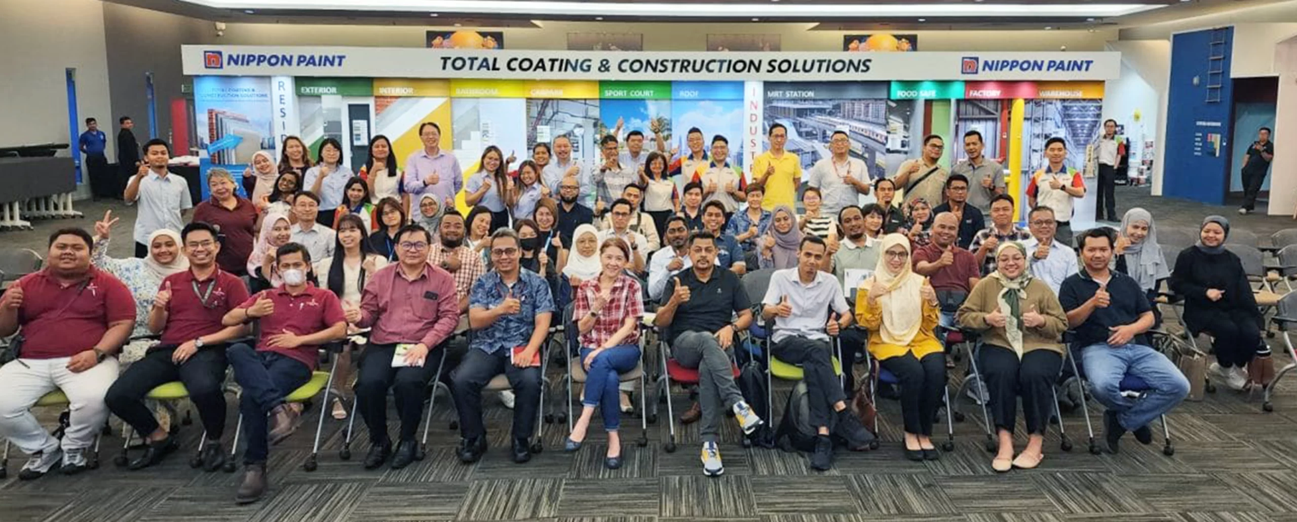 Group photo of Nippon Paint team members showcasing a collaborative spirit during a total coating and construction solutions event, with various product displays in the background.