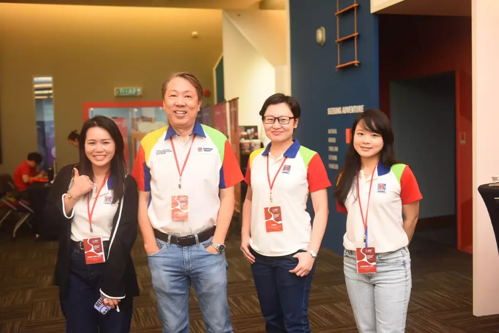 Team members of Nippon Paint pose together at an event, showcasing their branded shirts and engaging smiles. The setting features a modern interior, highlighting the company's vibrant culture and commitment to quality in paint solutions.