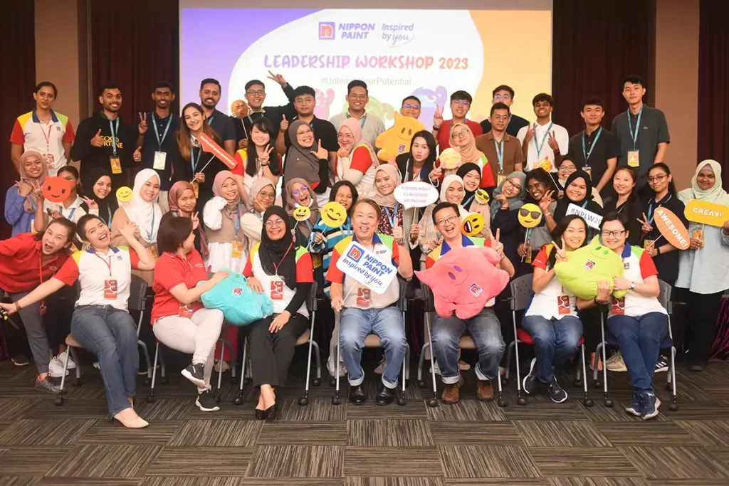Group photo of participants at the Nippon Paint Leadership Workshop 2023, showcasing teamwork and engagement with playful props, emphasizing the theme #UnleashYourPotential.