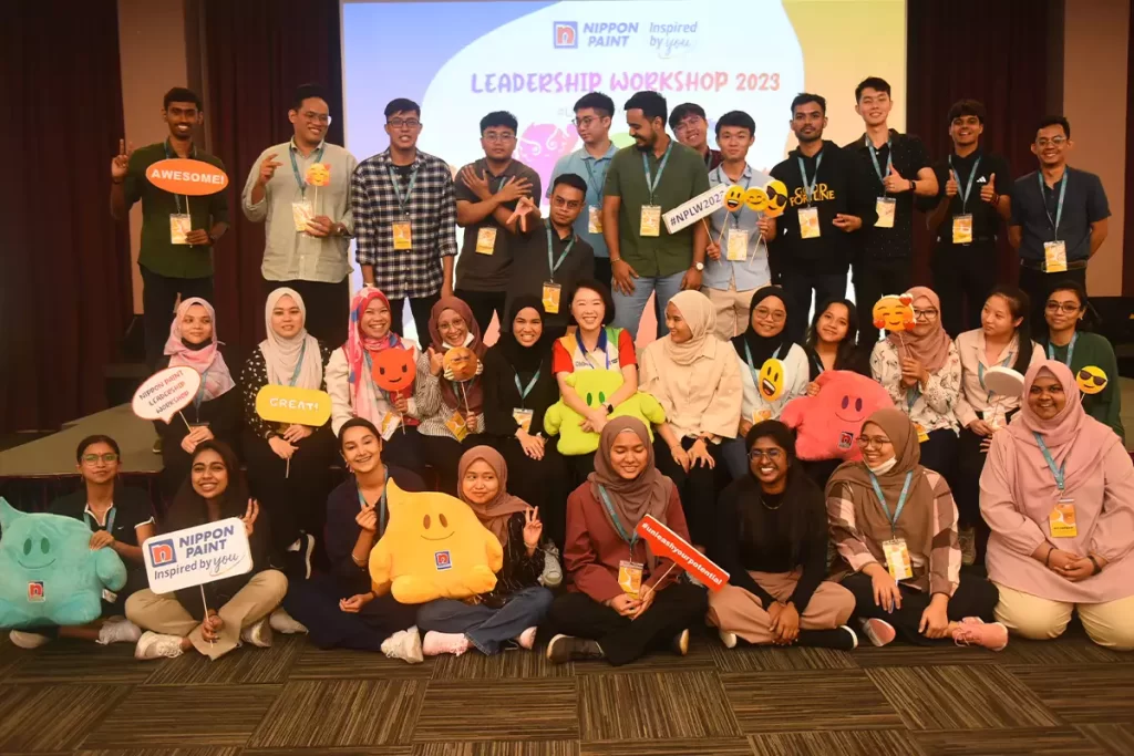 Group photo from the Nippon Paint Leadership Workshop 2023, featuring diverse participants holding playful props and smiling. The event promotes teamwork and leadership development, showcasing the Nippon Paint brand's commitment to inspiring potential.