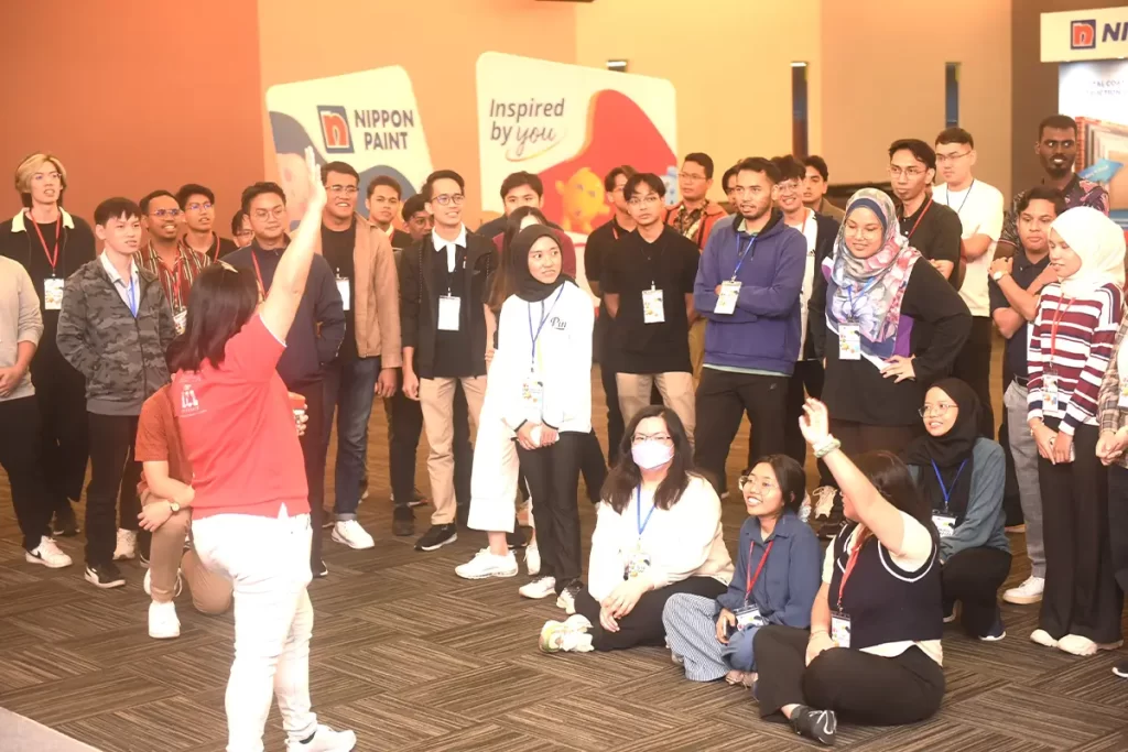 Group of young adults engaged in an interactive session at a Nippon Paint event, showcasing enthusiasm and teamwork, with branded displays in the background promoting Nippon Paint’s innovative products.