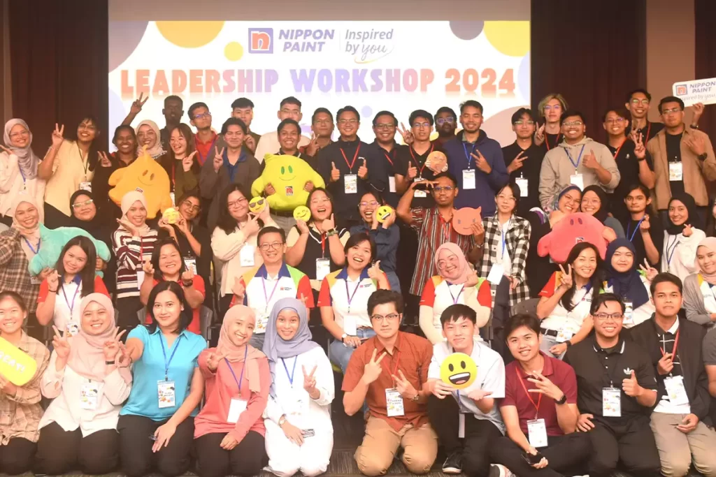 Group photo from the Nippon Paint Leadership Workshop 2024, featuring diverse participants smiling and posing with colorful props, showcasing teamwork and enthusiasm for leadership development.