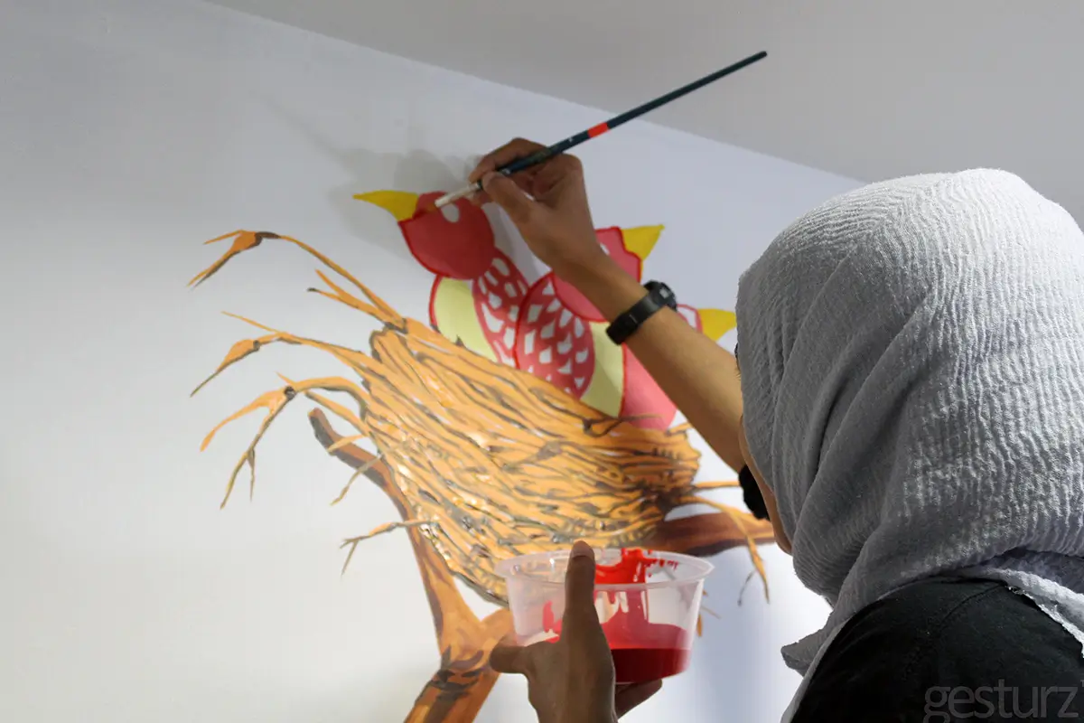 A person painting a colorful bird's nest mural on a wall using Nippon Paint products, showcasing artistic creativity and vibrant colors.