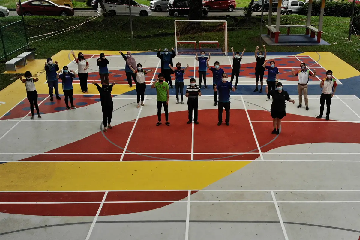 Group of participants wearing masks, standing on a colorful sports court painted with Nippon Paint products, engaging in a team activity while showcasing enthusiasm and teamwork.