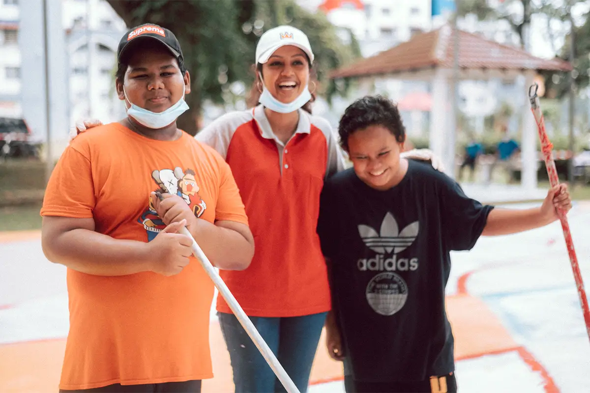 A community painting event featuring a woman and two children smiling while holding paint rollers, showcasing a vibrant playground revitalized with Nippon Paint products.