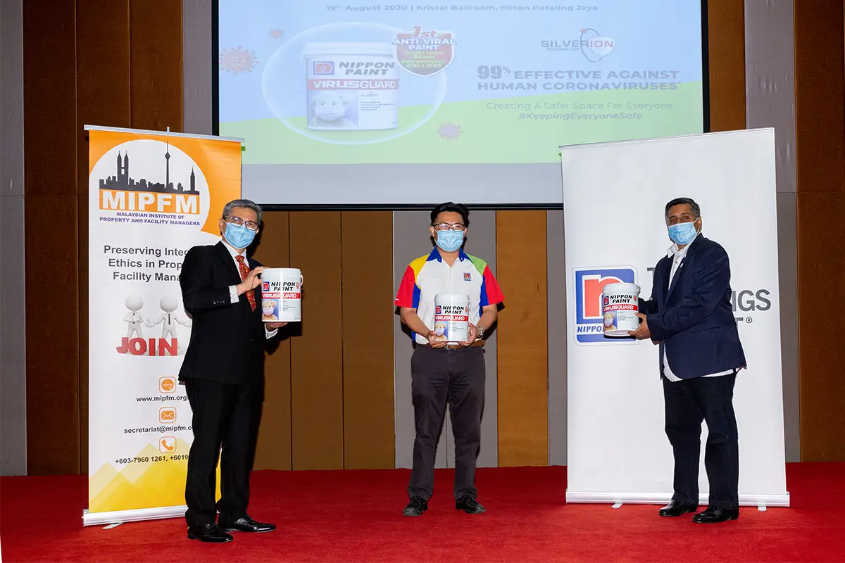 Event showcasing Nippon Paint's ViruGuard, an anti-viral paint effective against human coronaviruses, during the MIPFM conference at Hilton Petaling Jaya. Three presenters hold cans of the product, emphasizing its role in creating safer environments.