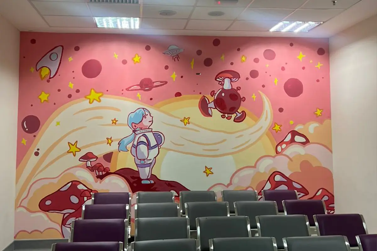 Colorful mural featuring a whimsical space theme with a girl in an astronaut suit, rockets, planets, and mushrooms, painted with Nippon Paint products. The mural adds a creative touch to the room, enhancing the atmosphere for gatherings or educational purposes.
