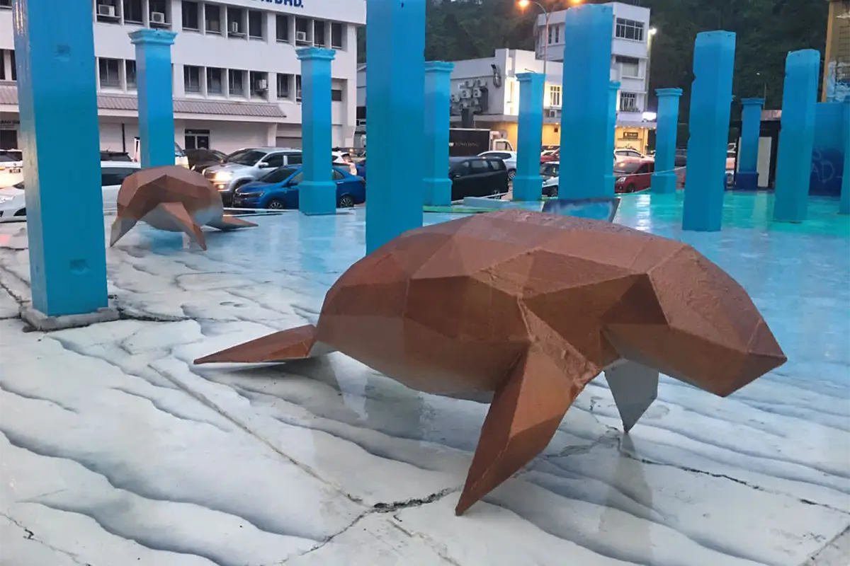 Sculptural sea creatures made of geometric shapes displayed on a vibrant blue and white surface, featuring Nippon Paint products for a striking visual effect. The artwork is set in an urban environment with parked cars and colorful pillars in the background.