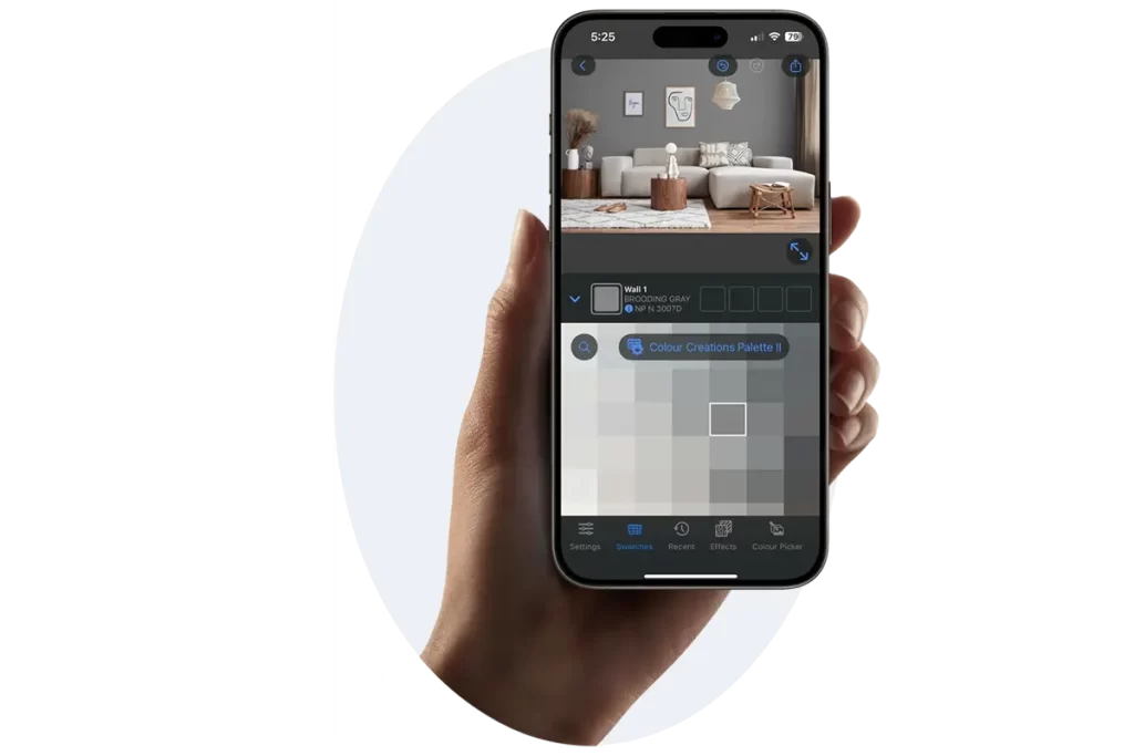 A hand holding a smartphone displaying the Nippon Paint Color Creations app, featuring a virtual room with a Brooding Gray wall and color palette options for home decor.