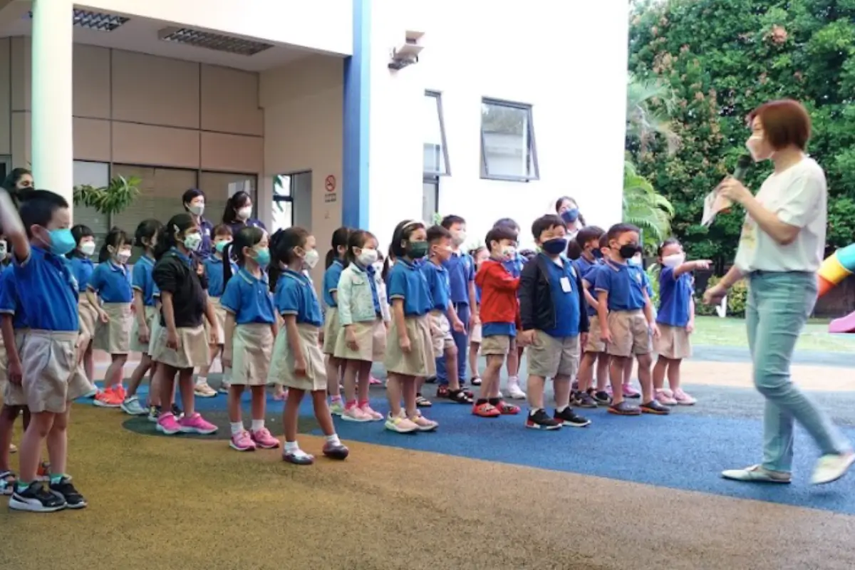 Children in blue uniforms participating in an outdoor activity at a school, with a teacher engaging them. The vibrant environment features safe play areas, showcasing the quality of Nippon Paint products used for maintaining bright and attractive school facilities.