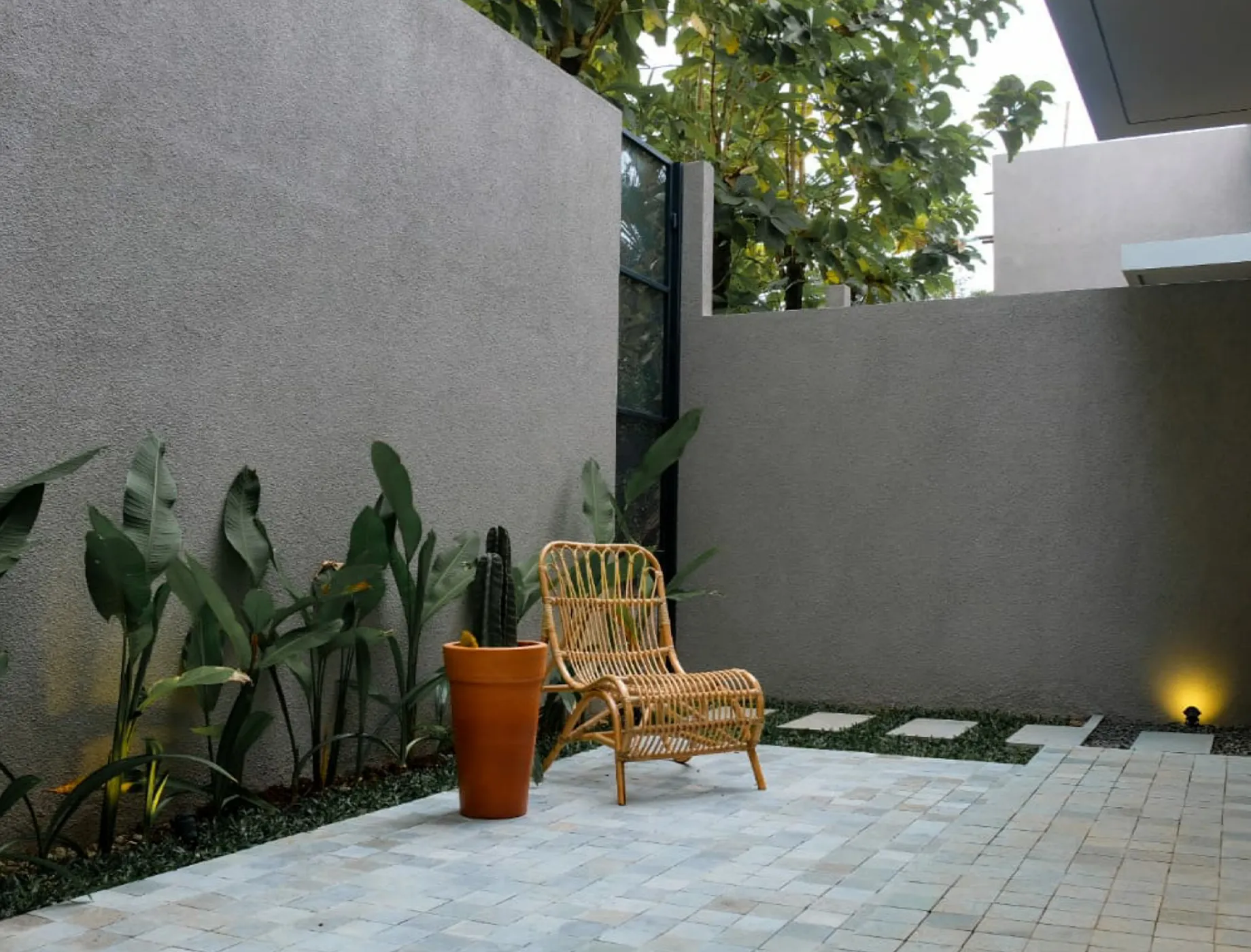 Stylish outdoor space featuring a wicker chair, a terracotta pot with a plant, and lush greenery. The textured gray wall, painted with Nippon Paint, complements the modern design elements, creating a serene atmosphere.