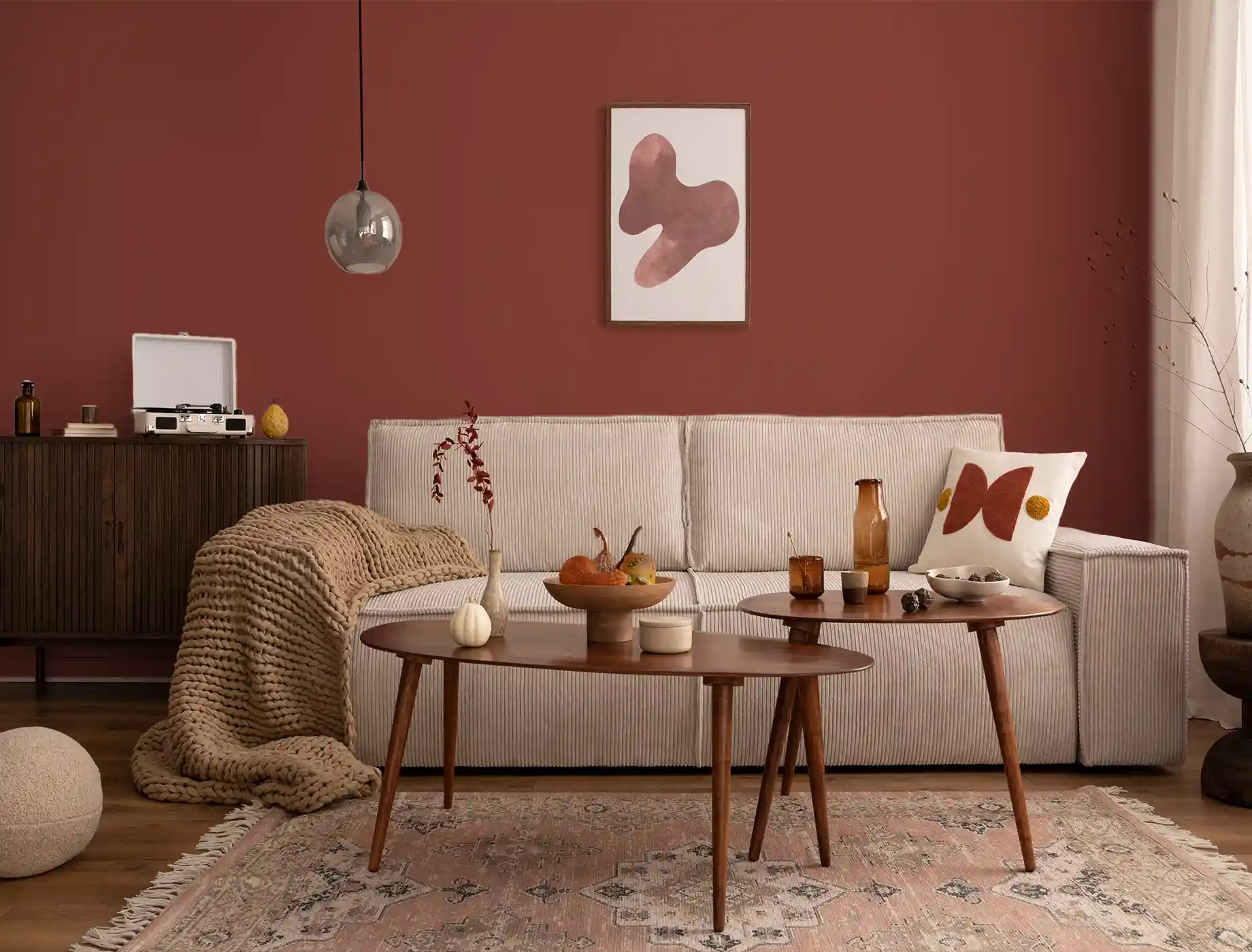 Modern living room featuring a Nippon Paint accent wall in rich terracotta, complemented by a cozy beige sofa, wooden coffee tables, and stylish decor elements. The space is enhanced with a soft throw blanket and artistic wall art, creating a warm and inviting atmosphere.
