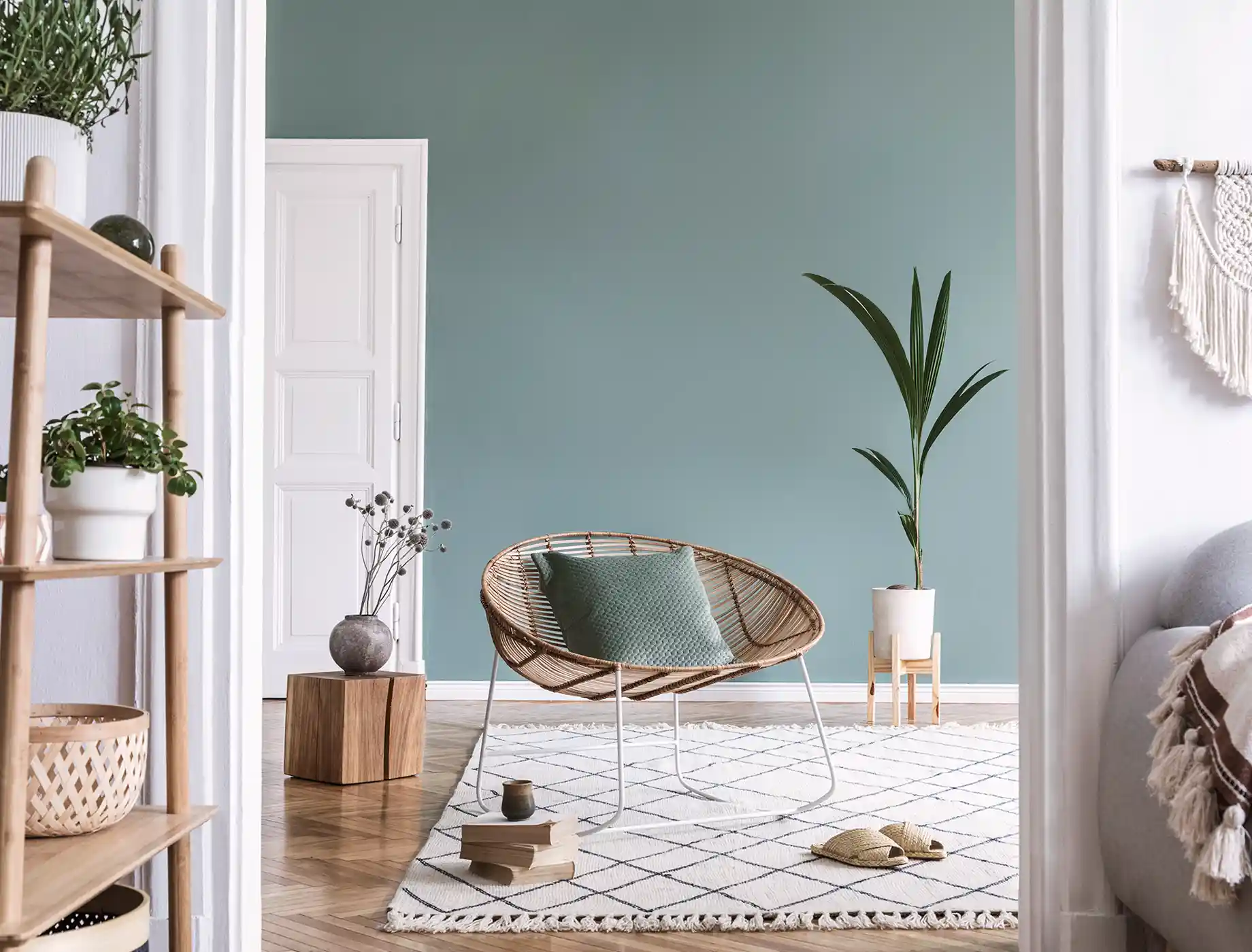 Stylish living room featuring a comfortable rattan chair and a soothing Nippon Paint teal wall. The space includes a decorative plant, a minimalist wooden table, and natural textures, creating a cozy and inviting atmosphere.